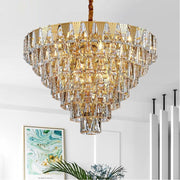 gold conical crystal chandelier illuminated with wall art and palm in back 