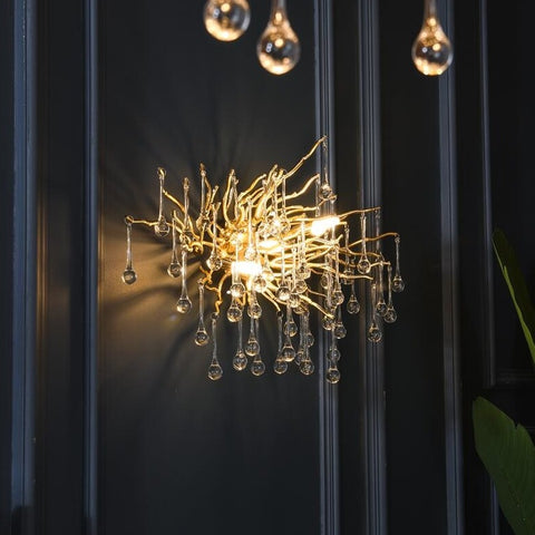 gold wall sconce with water drop crystals illuminated on a black paneled wall