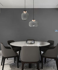 two glass minimalist lights with copper base with cord suspension hanging over contemporary dining room table with one long shape light and one wide light
