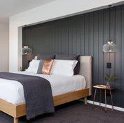 two glass minimalist lights with copper base with cord suspension hanging next to bed in front of shiplap feature wall
