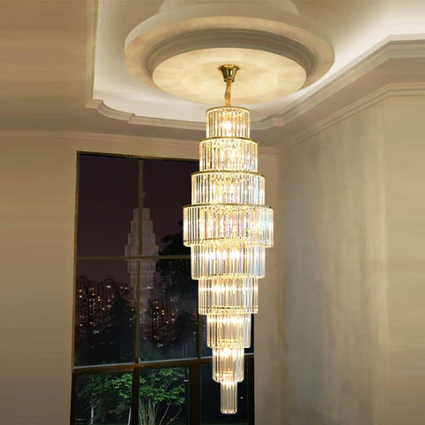 9 tier crystal chandelier hanging from high ceiling illuminated with night cityscape in background 