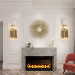 gold and clear crystal tubular wall sconces hanging on either side of a sun burst mirror over a lit fireplace