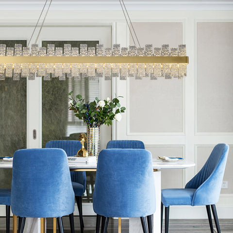 long rectangular water pattern glass chandelier with gold band hanging in dining room with blue chairs