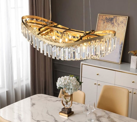 gold chandelier with long body and rectangular crystals hanging down in a boat shape hung over marble top table